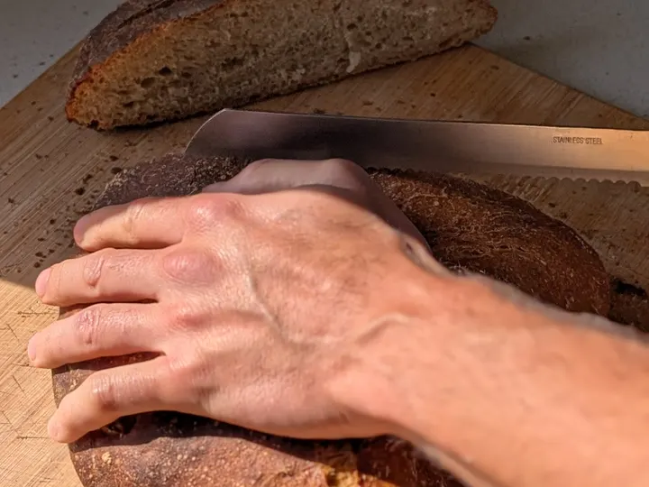 Mà que talla un pa de crosta fosca amb un ganivet de pa