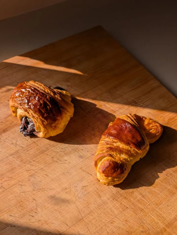 Un pain au chocolat i un croissant daurats sobre una taula de fusta, amb llum de tarda